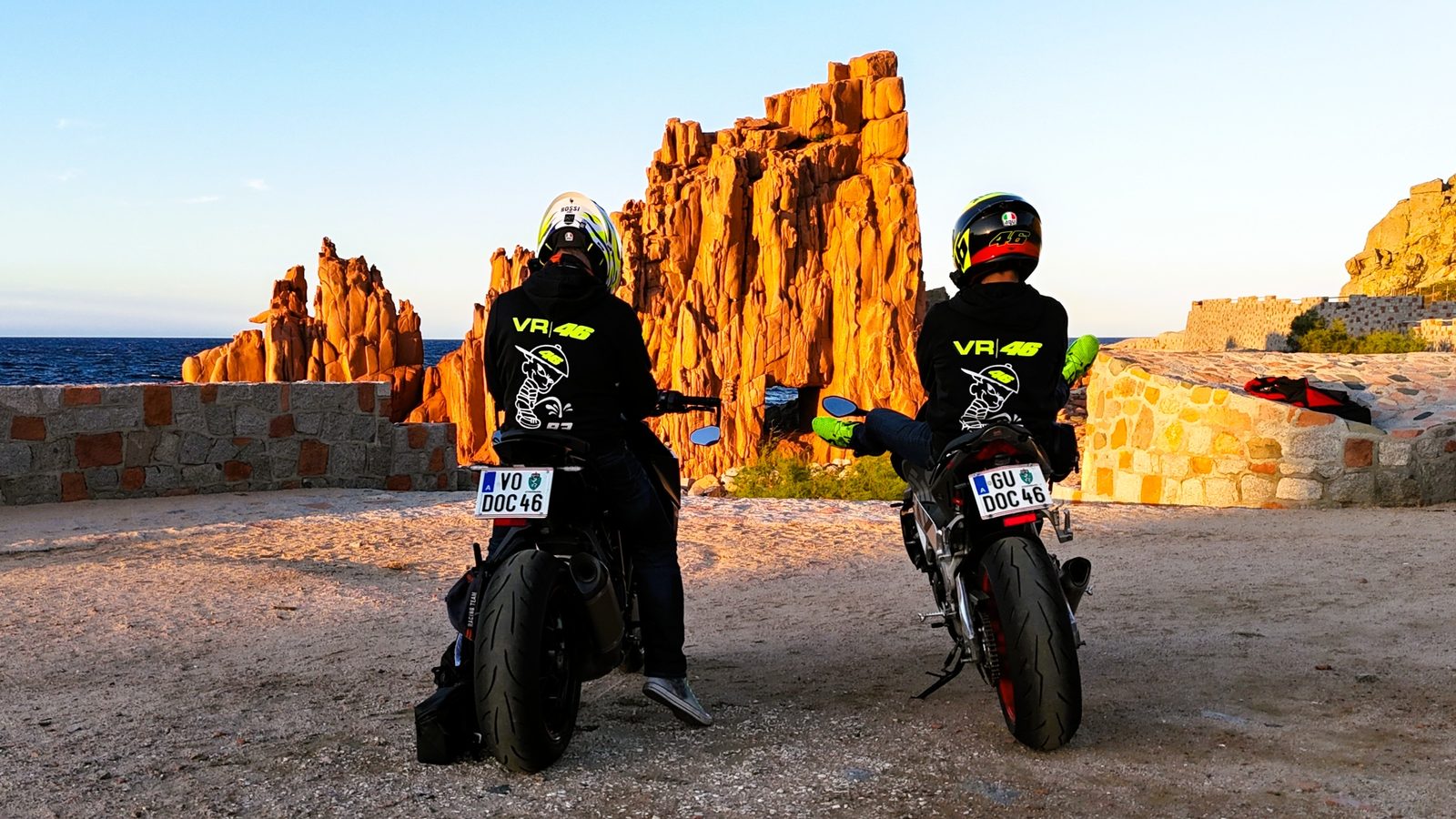 Zwei Motorräder vor roten Felsen am Meer bei Sonnenuntergang